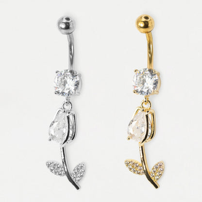 Two rose-shaped belly button rings shown side by side on a plain light background. One is silver-toned and the other is gold-toned, both featuring a clear faceted gemstone, a teardrop-shaped clear gemstone, and leaf details paved with small clear stones.