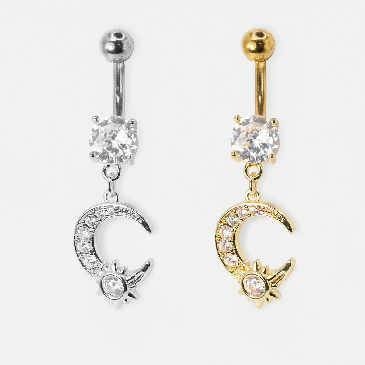 A pale grey image showing two belly bars side by side in steel and gold steel featuring a round clear crystal and a dangling pavé-set crescent moon charm with a nested crystal sun motif by Kingsley Ryan Wholesale