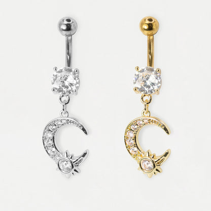 A pale grey image showing two belly bars side by side in steel and gold steel featuring a round clear crystal and a dangling pavé-set crescent moon charm with a nested crystal sun motif by Kingsley Ryan Wholesale