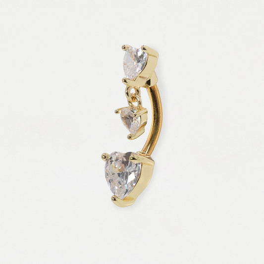 Gold curved barbell belly button ring with three dangling clear heart-shaped and marquise-cut crystals, shown on a light gray background.